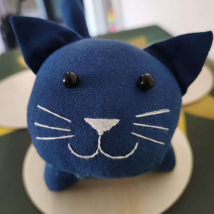 Close-up of plant dyed indigo cat toy, showcasing facial features and embroidery details